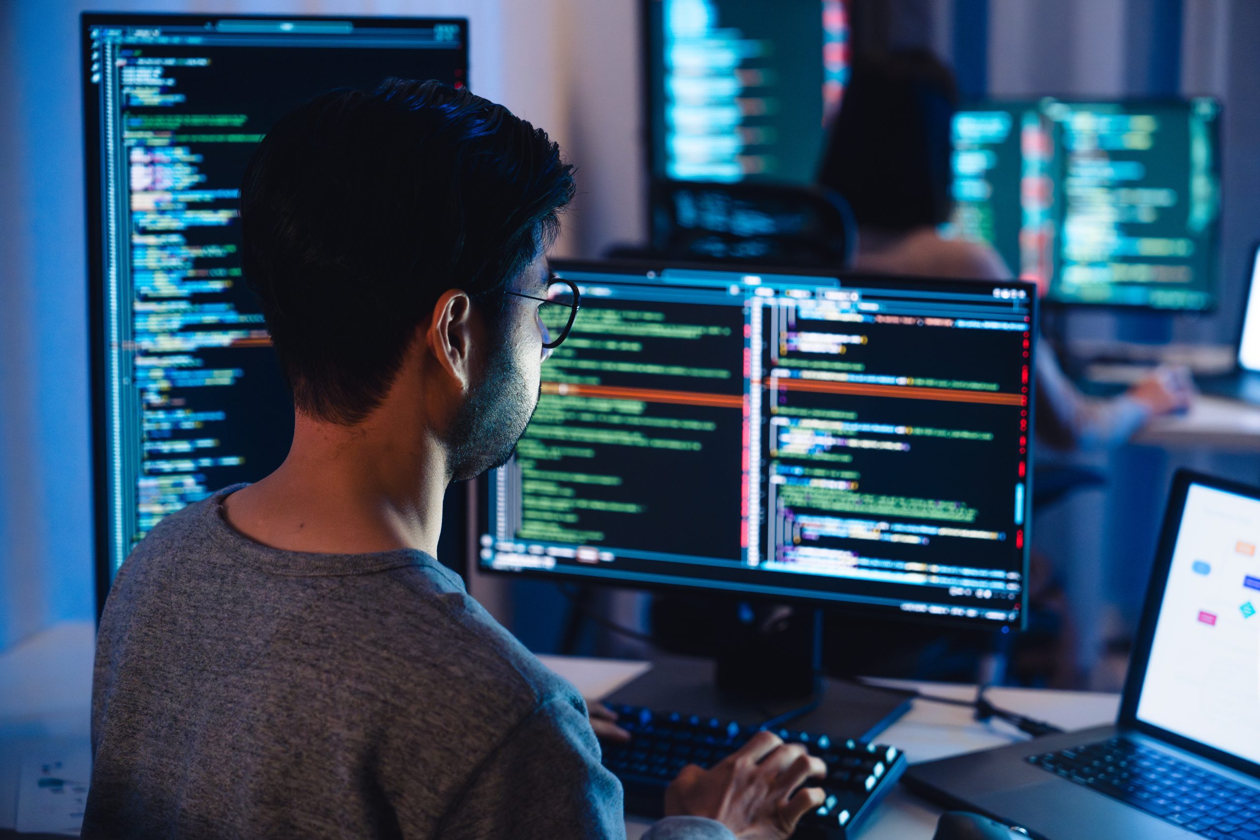 Asian software developers working on multiple screens displaying code and application diagrams at night in modern office